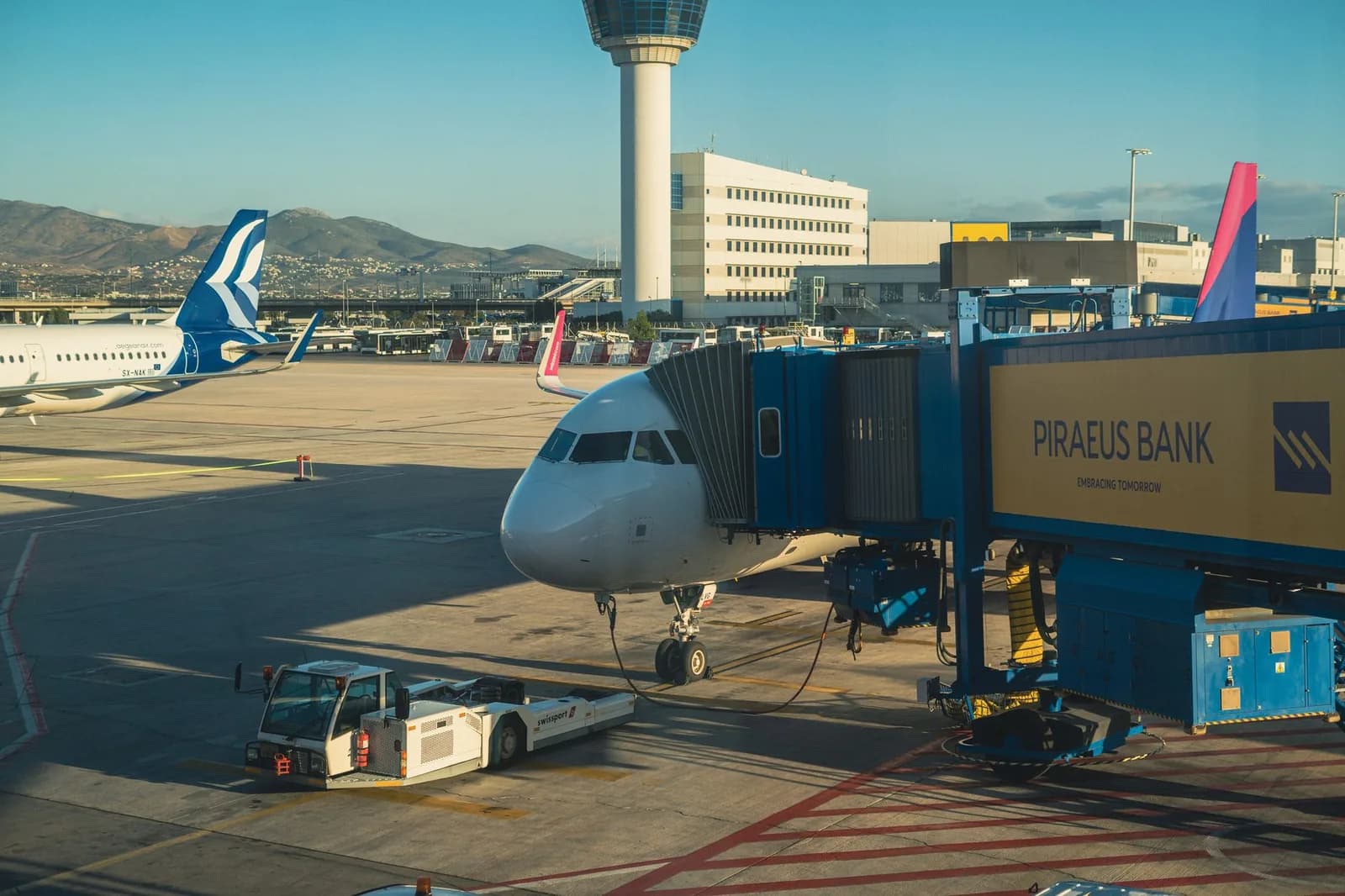 Aircraft on stand at Athens International Airport with the control tower and the hills of Attica behind