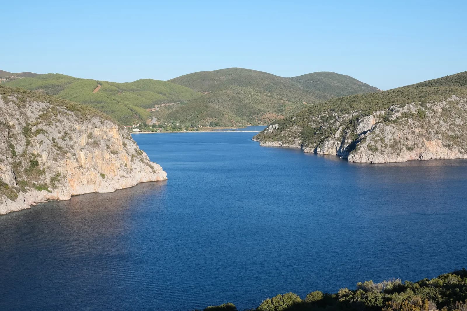The narrow entrance to Porto Koufo, the deep natural harbour between limestone cliffs on the southern tip of Sithonia, Halkidiki, with the village and wooded hills at the far end
