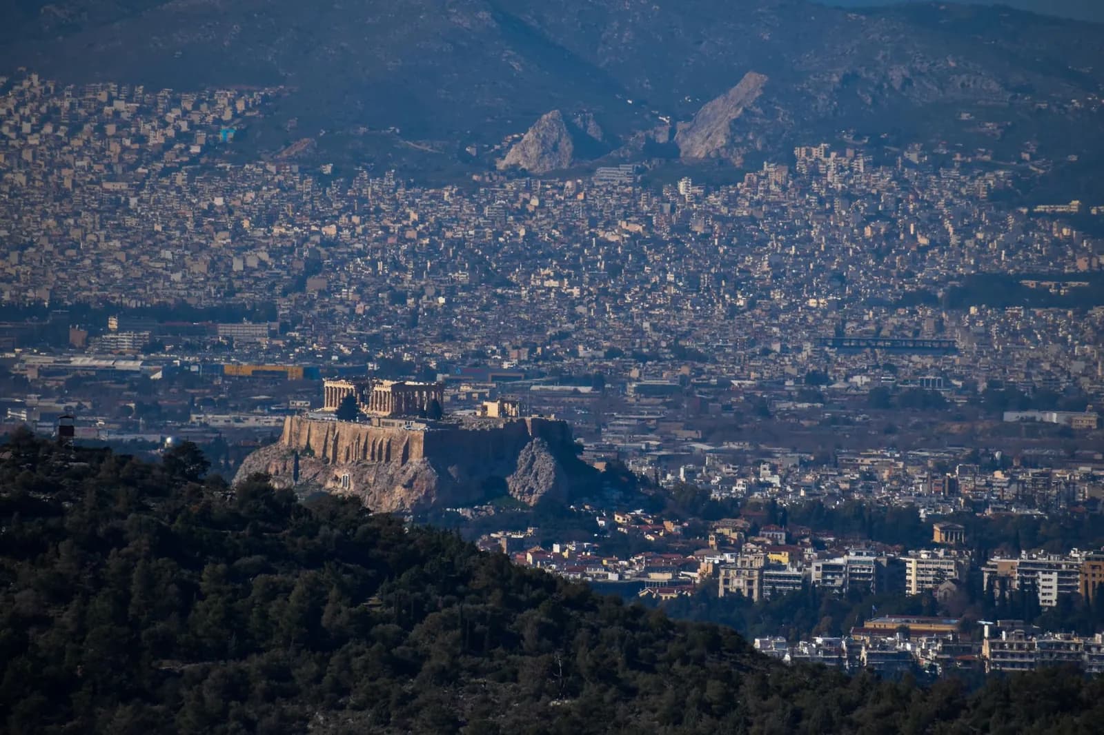 The Acropolis and the Parthenon rising above the rooftops of central Athens, with the city basin and Mount Hymettus behind