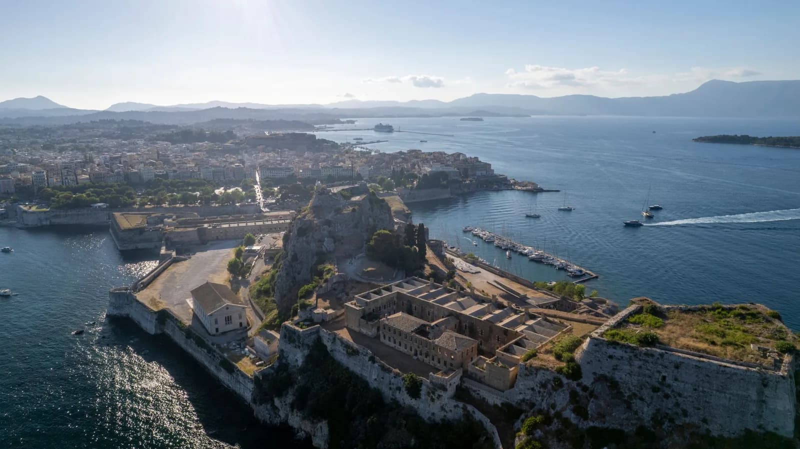 The Old Fortress and the old town of Corfu from the air, with the marina, Vidos island and the mountains of the mainland behind