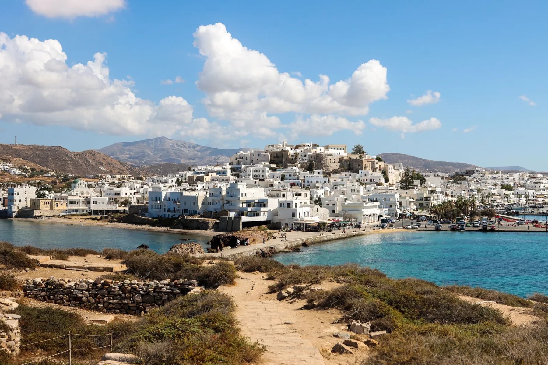 Naxos Chora seen across the water from the Portara causeway, with the Venetian kastro above the white town and the mountains of the island behind