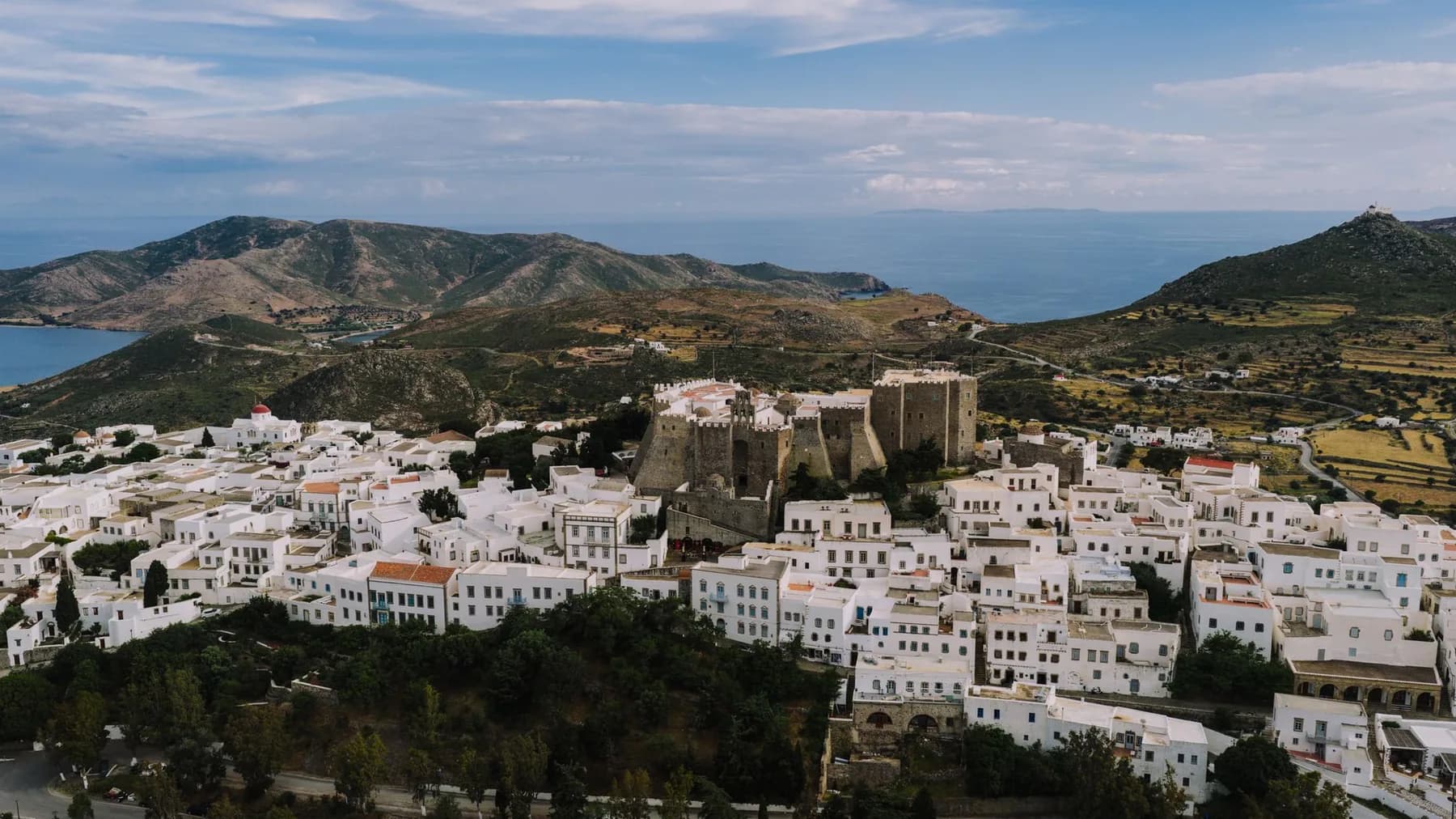 The fortified stone monastery of Saint John standing above the white flat-roofed houses of the Chora on Patmos, with bare hills and the sea beyond