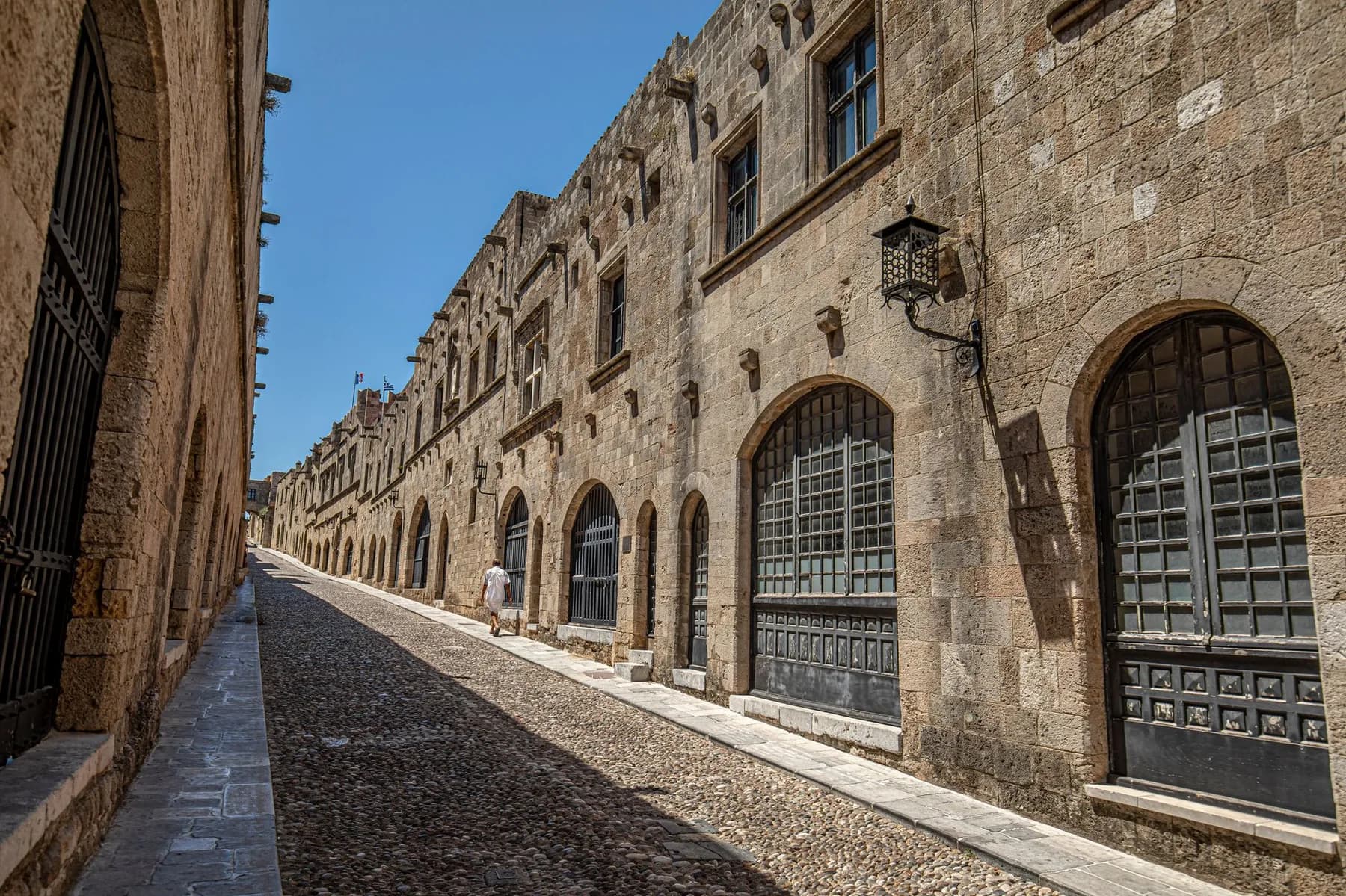 The cobbled Street of the Knights in Rhodes Old Town, lined with the stone façades and arched doorways of the medieval inns, almost empty in the midday sun