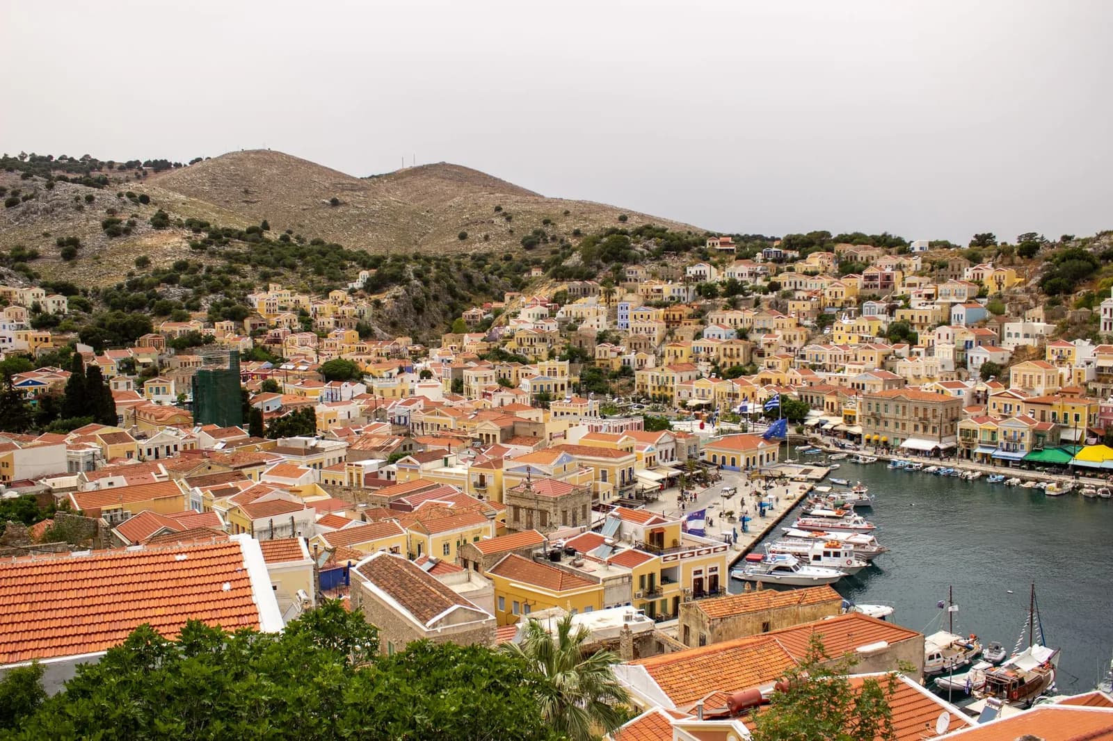 The harbour of Gialos on Symi seen from the hillside above, with tiers of ochre neoclassical houses and boats along the quay