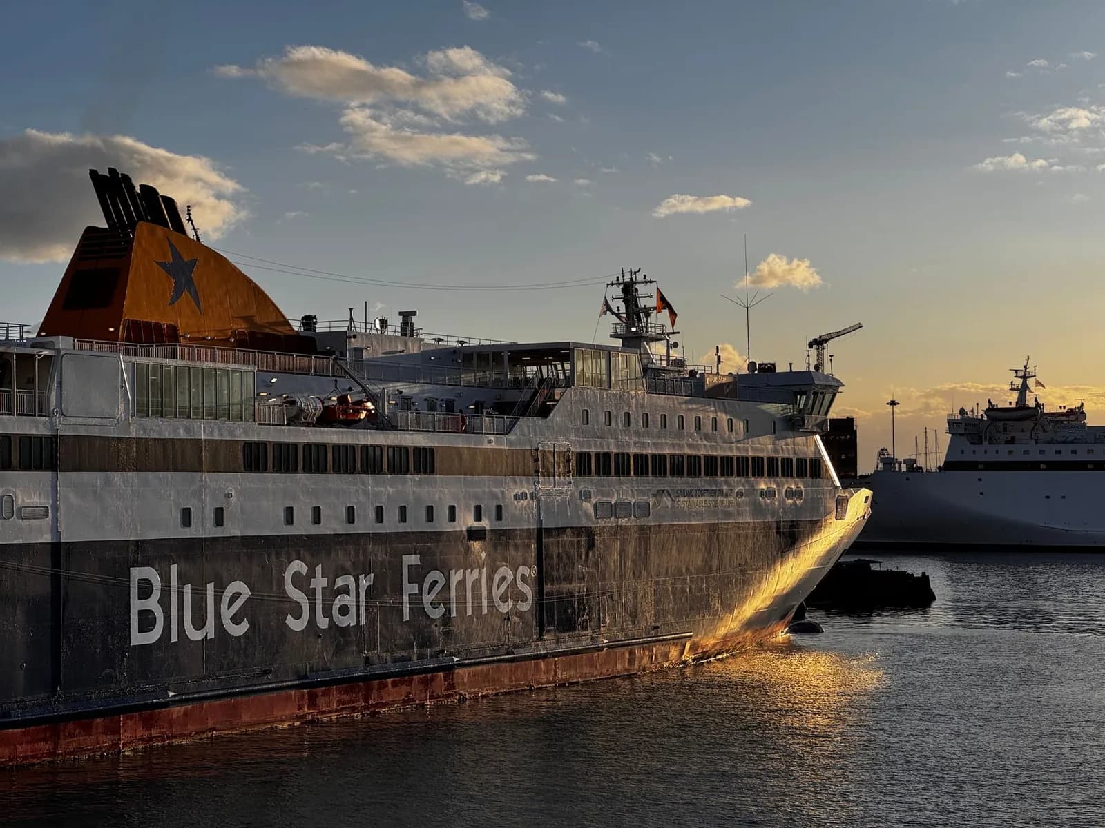 A Blue Star Ferries ship berthed at the quay in Piraeus at first light, with a second ferry moored further along the port behind it