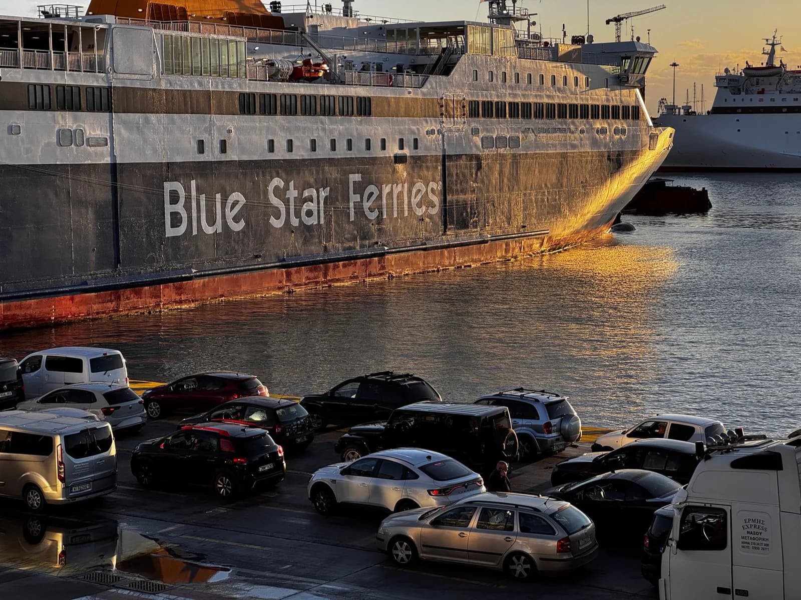 Cars queuing on the quay at Piraeus in the evening beside a conventional ferry loading for the overnight crossing to Crete