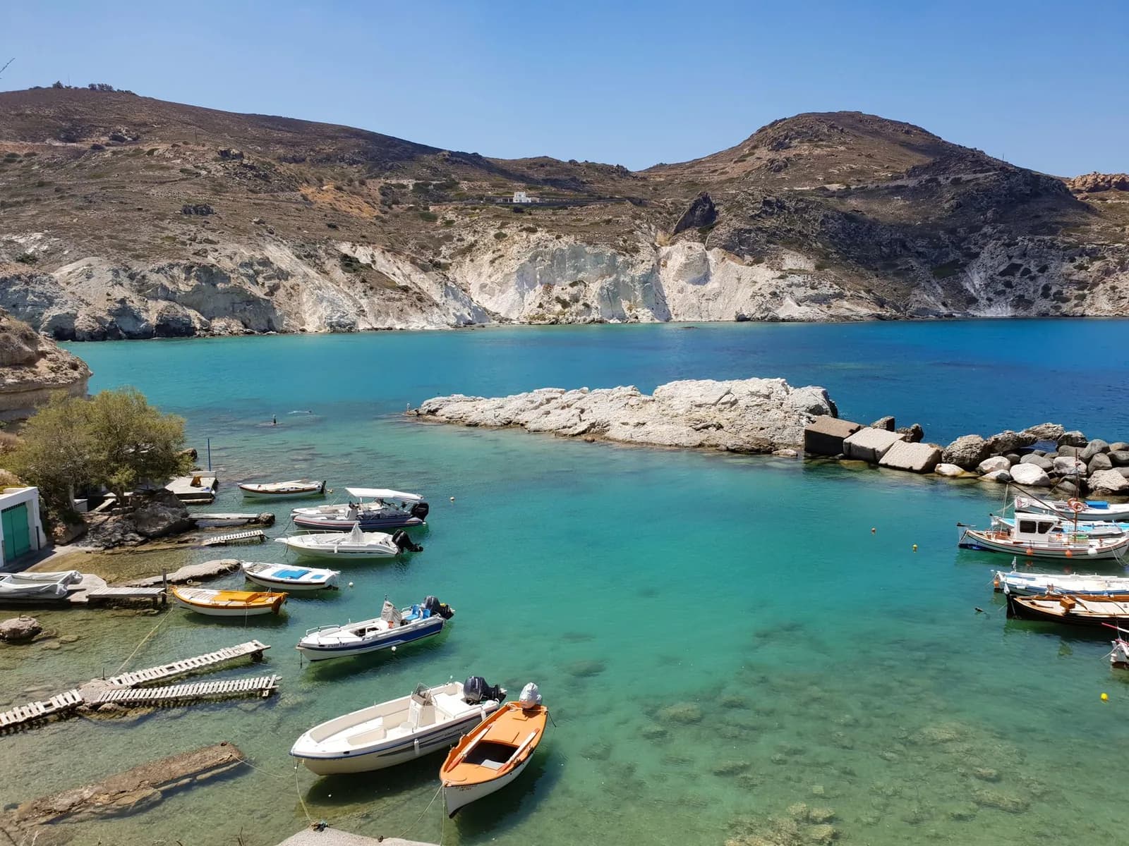 A small fishing cove on Milos, with pale volcanic cliffs and bare hills rising behind the moored boats