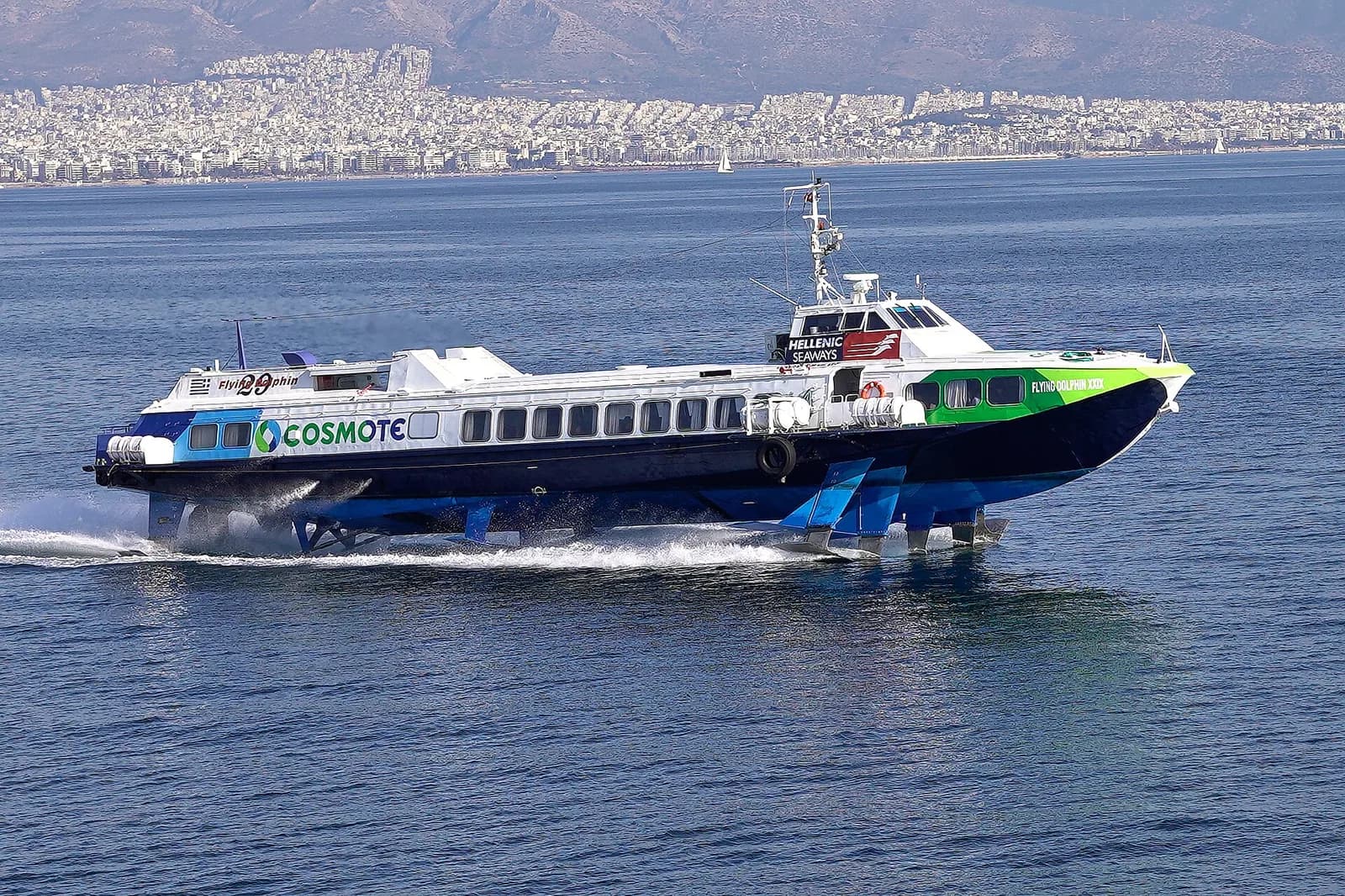 Hellenic Seaways Flying Dolphin hydrofoil riding on its foils in the Saronic Gulf, with the Athens coastline behind