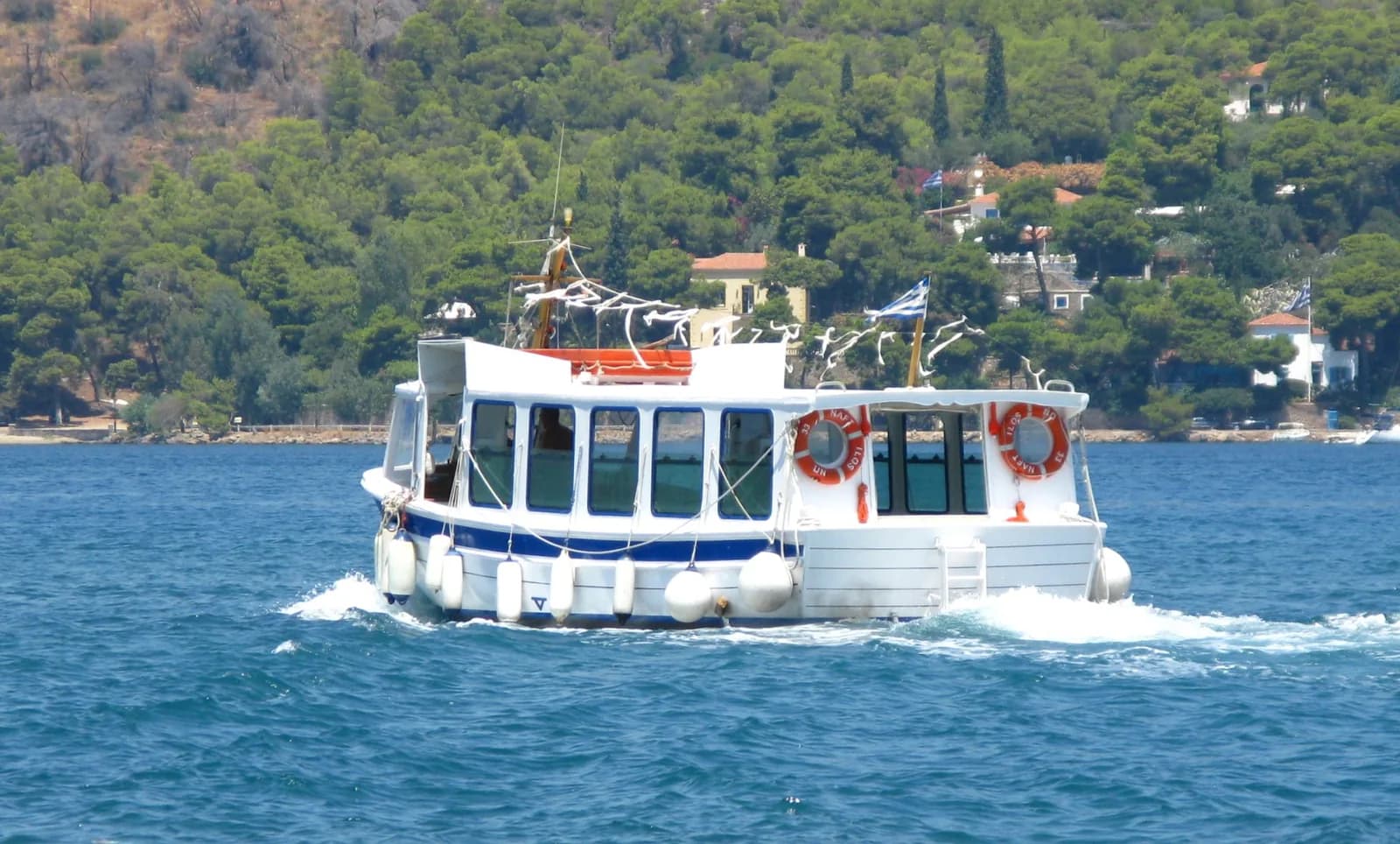 Small passenger boat crossing the narrow strait between Galatas and Poros, with the pine-covered Peloponnese shore behind