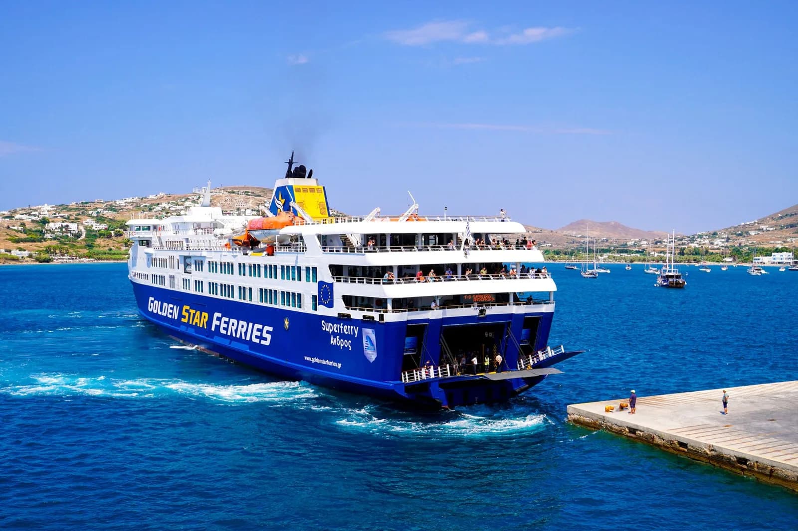 A Greek ferry reversing on to the quay of a Cycladic port with its stern ramp lowered