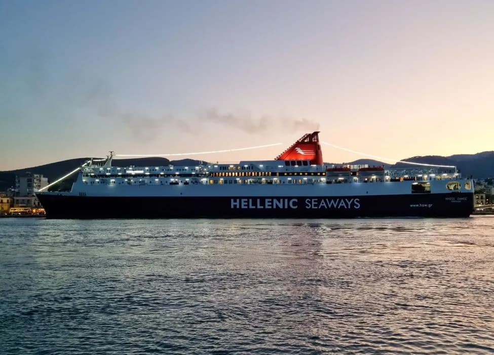 A Hellenic Seaways conventional ferry lit up at dusk off a Greek island port