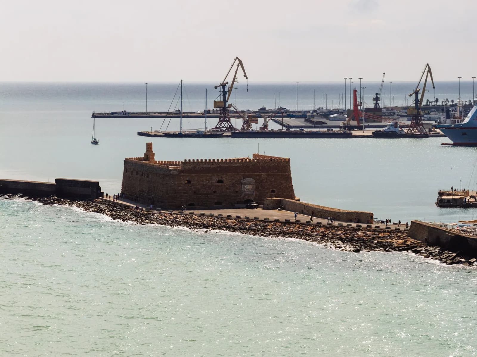 The Koules fortress on the mole at Heraklion, with the commercial ferry quays, gantry cranes and a berthed ship behind it, Crete