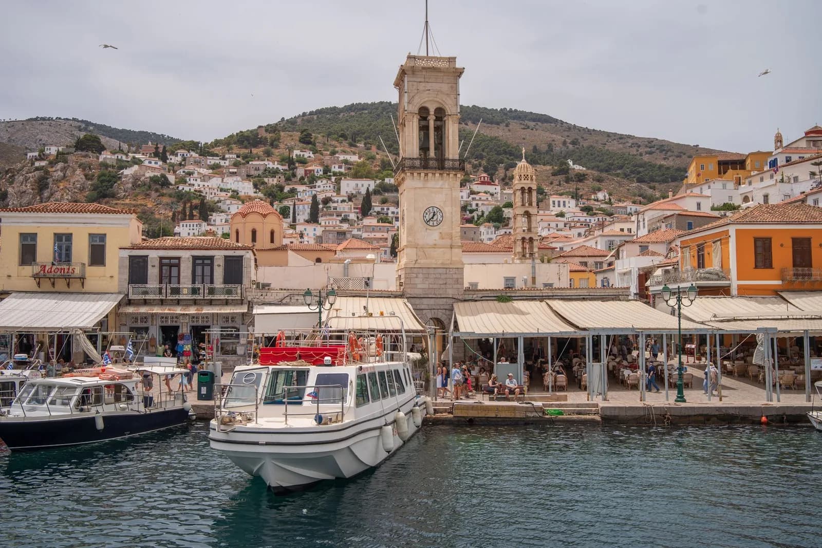 Hydra harbour front with the clock tower, stone houses climbing the hillside and a white boat at the quay