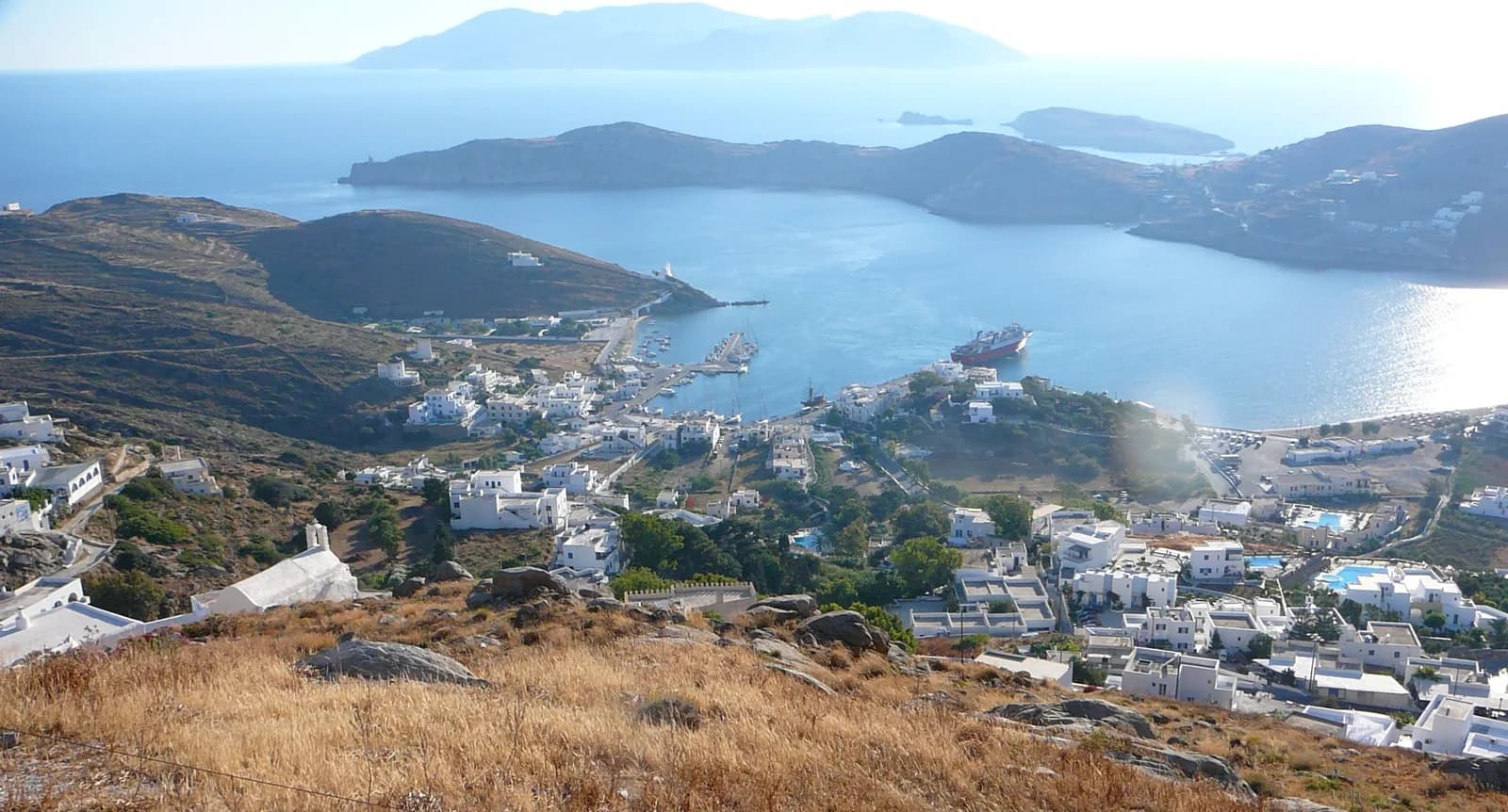 The bay and port of Ios seen from the hillside below Chora, with a ship in the harbour and Sikinos on the horizon