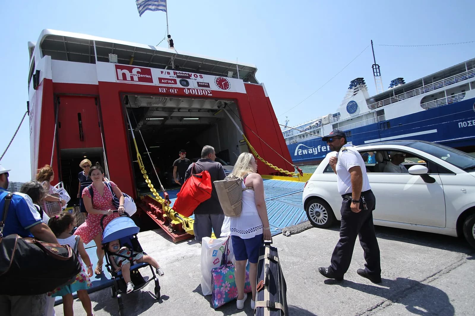 Passengers with luggage and a pushchair walking off a ferry ramp at the port of Piraeus, with a Blue Star ferry behind