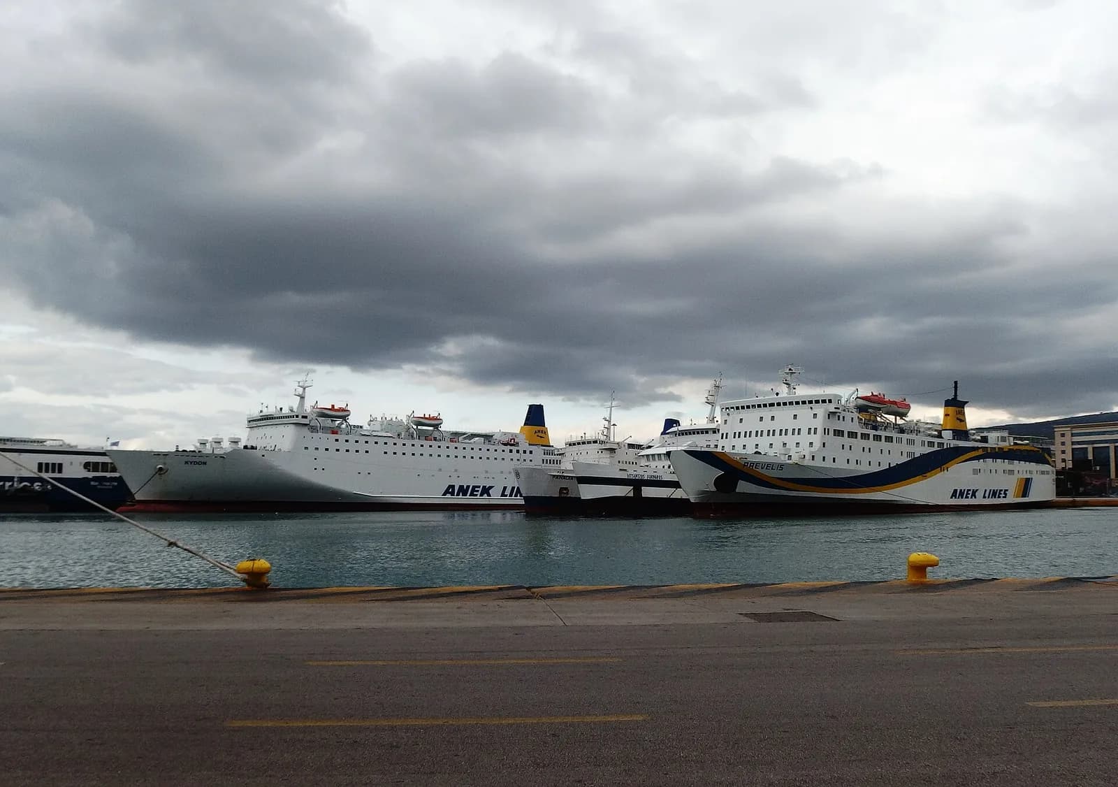 Ferries of ANEK and Minoan Lines moored along a quay at the port of Piraeus, Athens, under a cloudy sky
