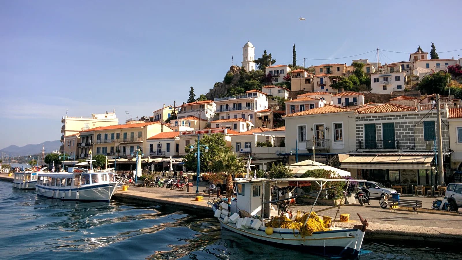 Poros town seen from the harbour, with the clock tower on the hill above the waterfront houses and fishing boats moored on the quay