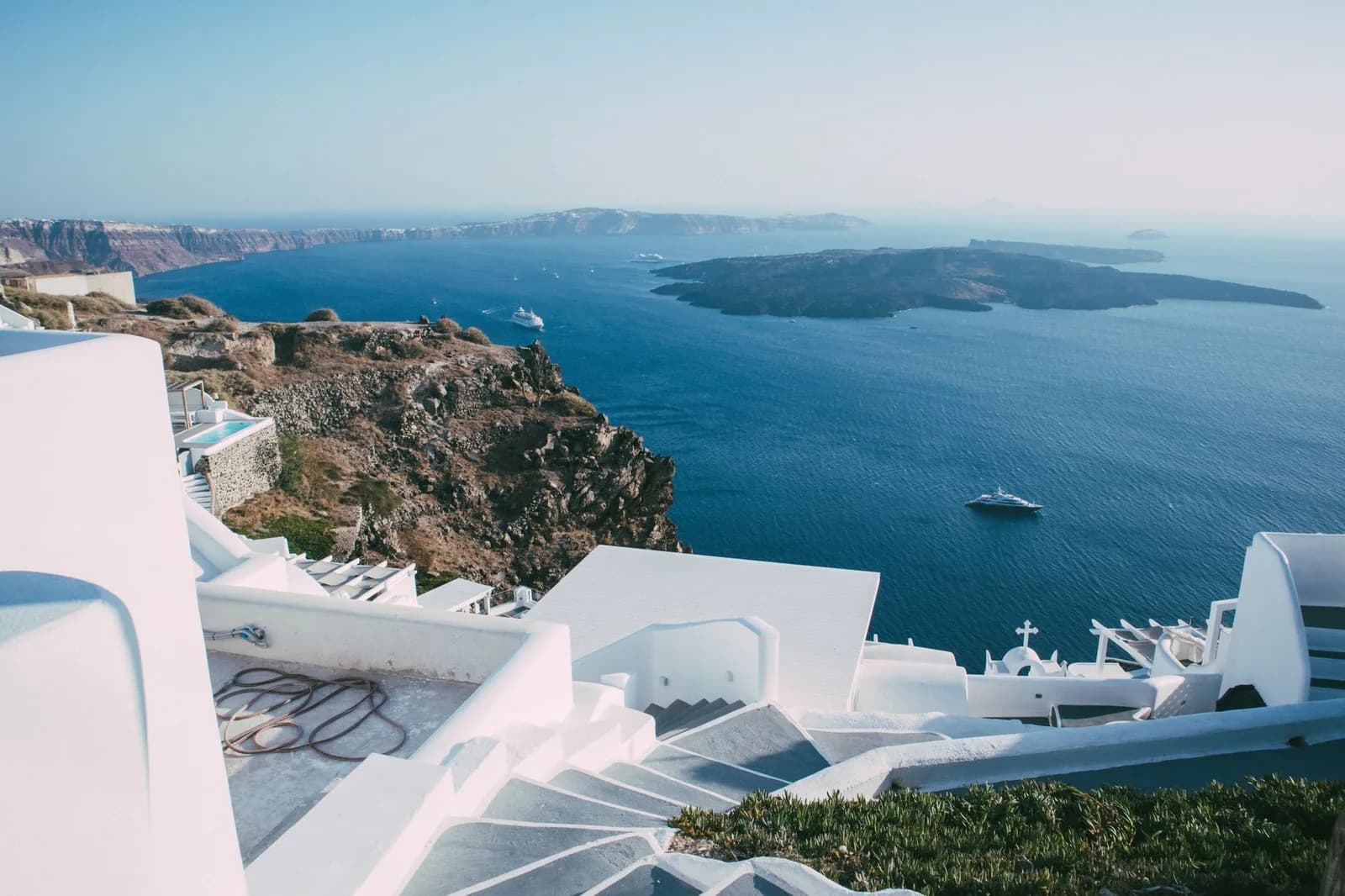 Whitewashed stairs stepping down between hotel terraces on the Santorini caldera cliff, with Nea Kameni in the distance