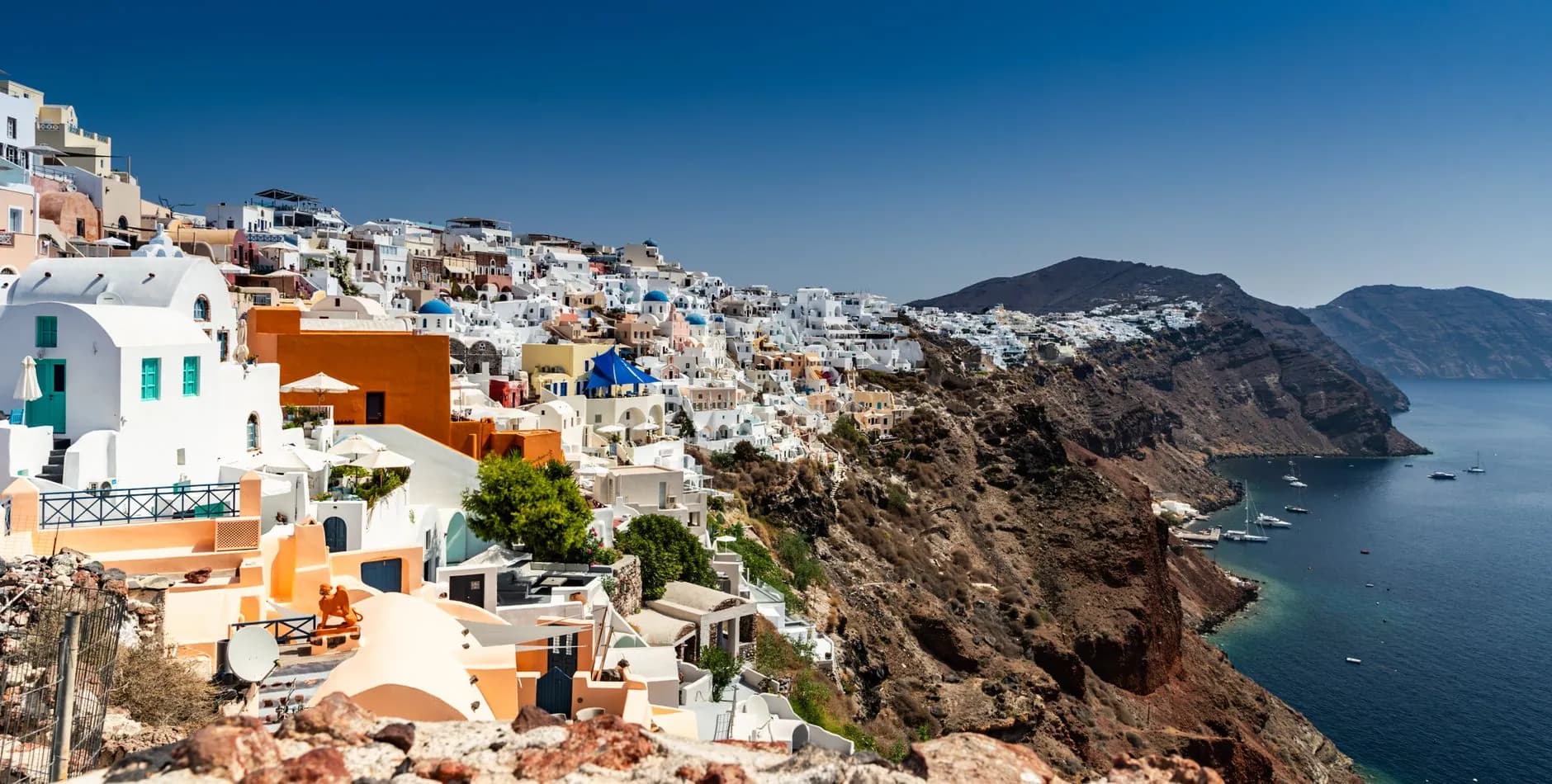 The village of Oia strung along the top of the Santorini caldera cliff, with yachts anchored in the water far below