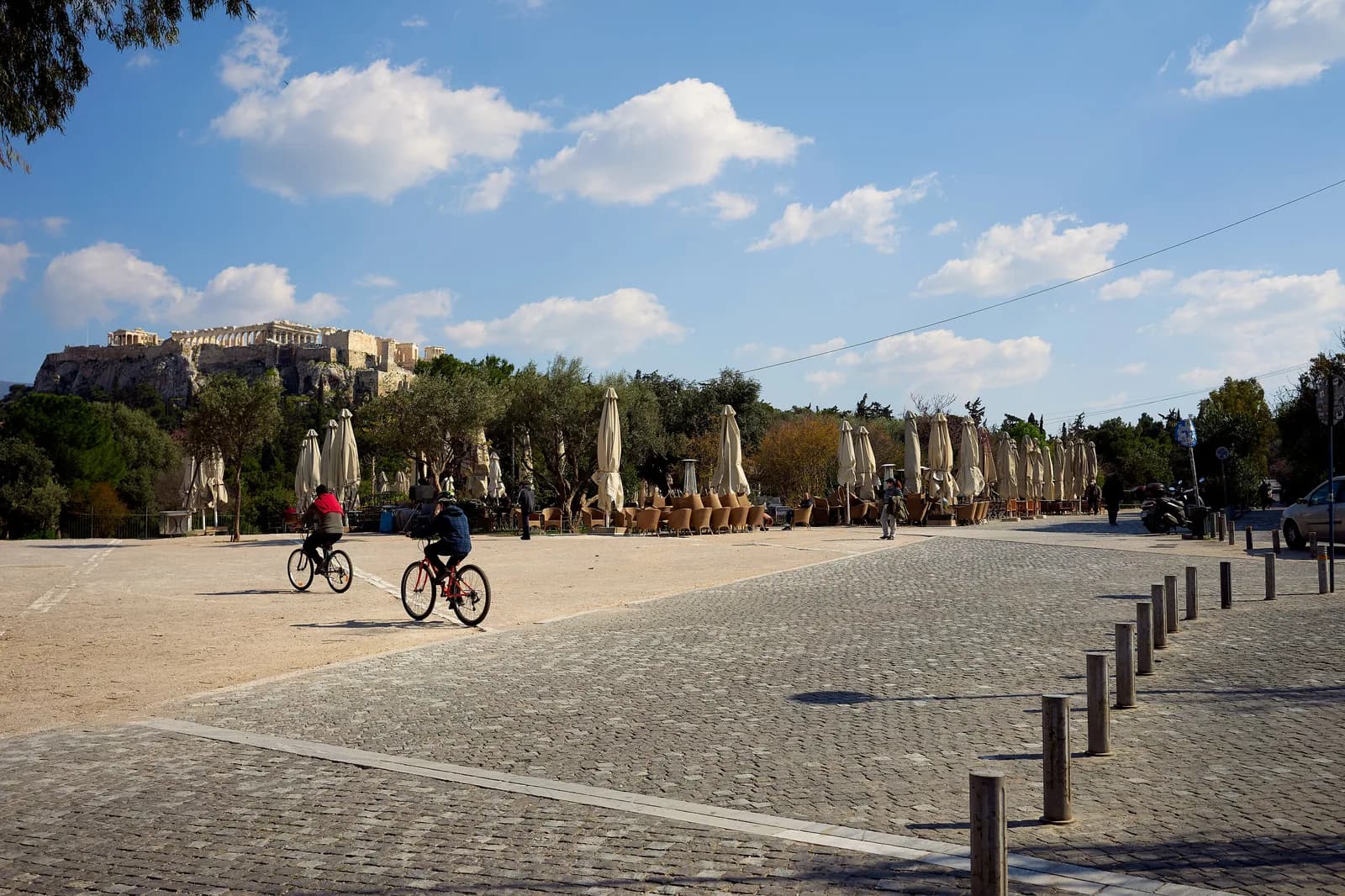 The Apostolou Pavlou pedestrian promenade in Thissio, Athens, with cyclists, furled café umbrellas and the Acropolis in the distance
