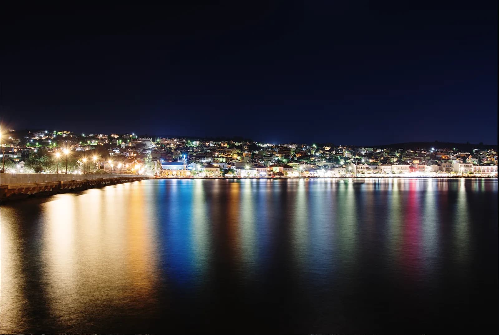 Argostoli at night on Kefalonia, the lit waterfront and the houses on the hillside reflected in the still water of the Koutavos lagoon, seen from the De Bosset causeway
