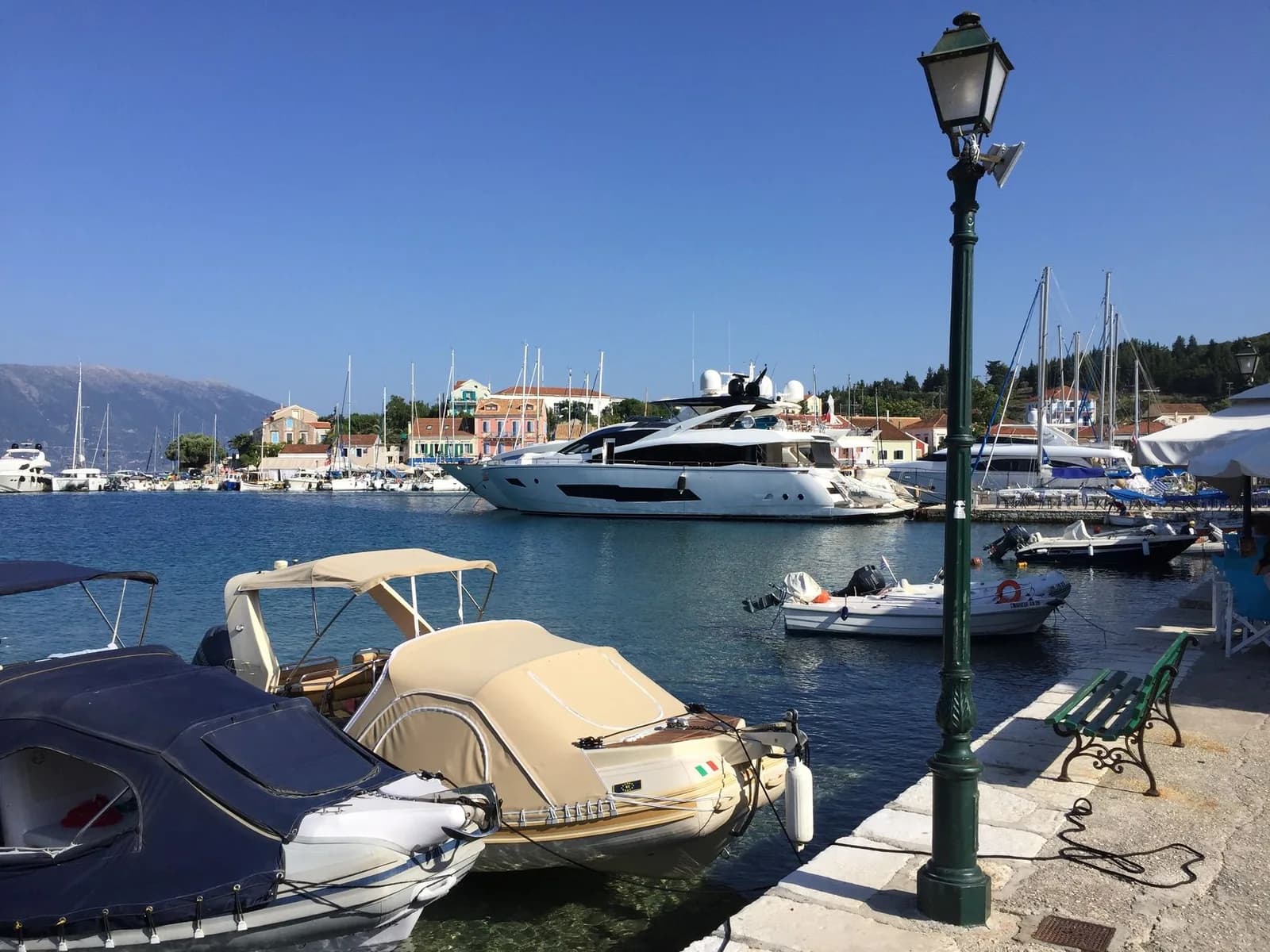 The harbour at Fiskardo on Kefalonia, small boats and a large motor yacht moored in front of the pastel waterfront houses, with the mountains across the channel behind