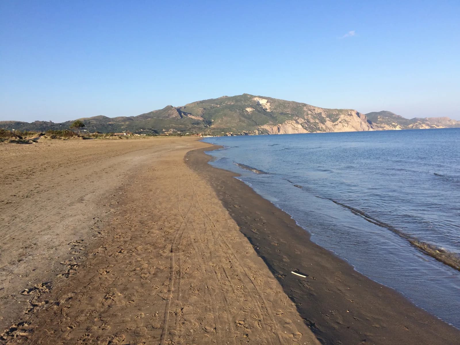 Empty stretch of sand at the Kalamaki end of Laganas Bay, Zakynthos, with Mount Skopos and its pale cliffs rising beyond the calm water