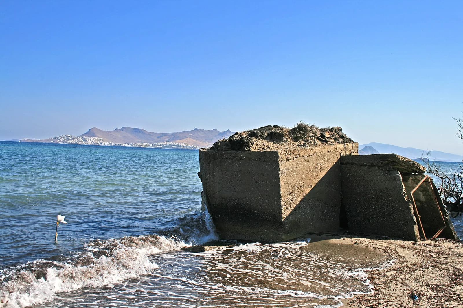 A concrete wartime bunker half in the waves on Lambi beach, Kos, with the Turkish coast and the houses of the Bodrum peninsula across the water
