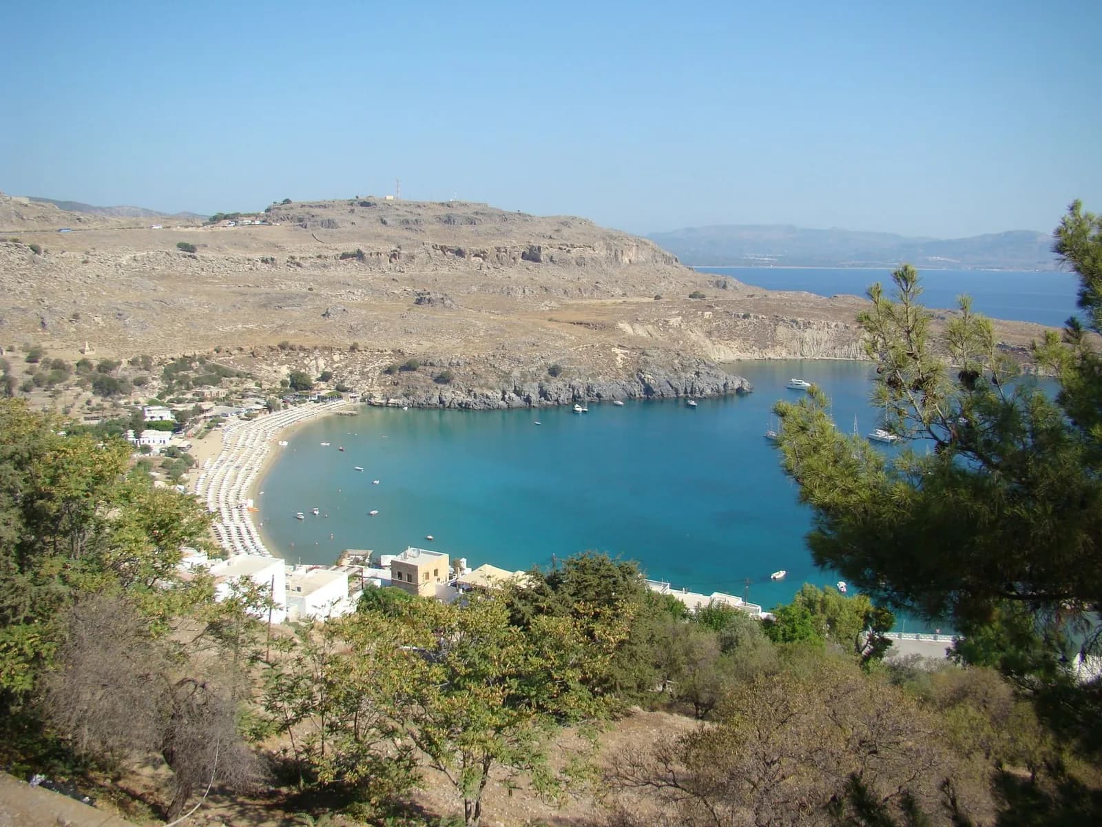 The sheltered sandy bay at Lindos on the east coast of Rhodes, with sunbeds along the shore and boats at anchor