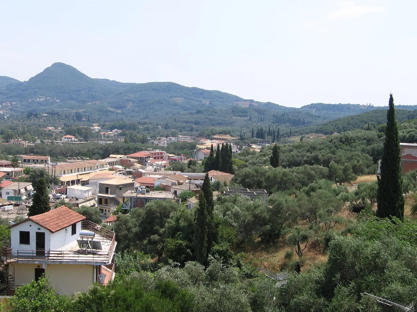 Moraitika on the south-east of Corfu seen from the hillside, low houses and hotels among olive trees and cypresses with green hills behind