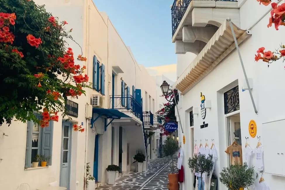 A marble-paved lane in the old town of Parikia on Paros, hotel signs and shops under bougainvillea