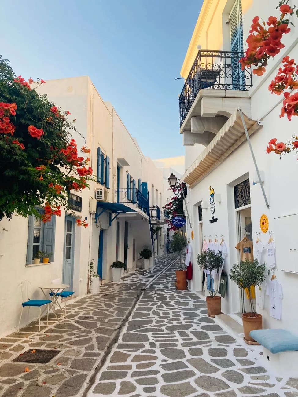 A marble-paved lane in the old town of Parikia on Paros, hotel signs and shops under bougainvillea