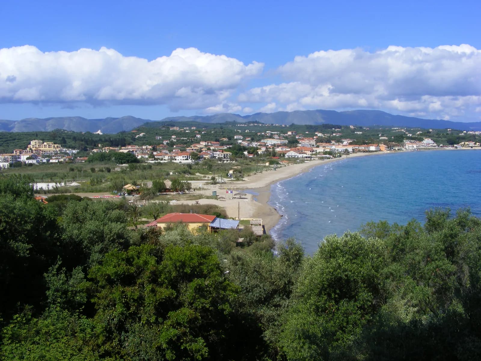 Tsilivi bay on the east coast of Zakynthos seen from the hillside, a curving sandy beach backed by low-rise hotels with mountains on the horizon