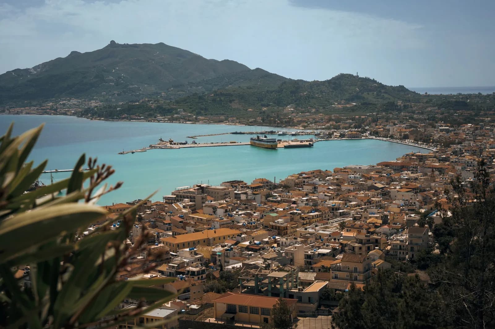 Zakynthos Town from Bochali hill, terracotta rooftops running down to the turquoise harbour, a ferry at the mole, and Mount Skopos across the bay
