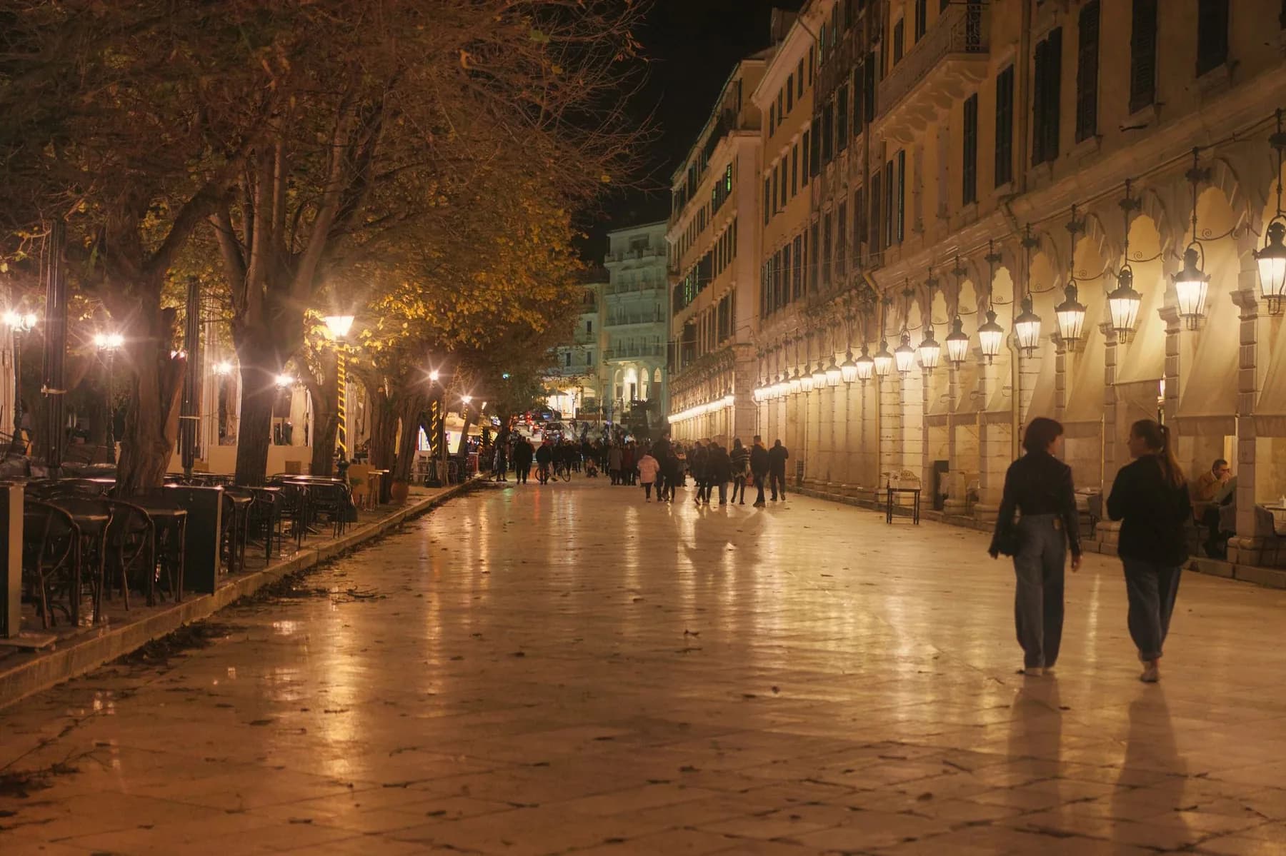 The arcaded terrace of the Liston in Corfu Town lit at night, with its row of lanterns on the right and the trees of the Spianada esplanade on the left