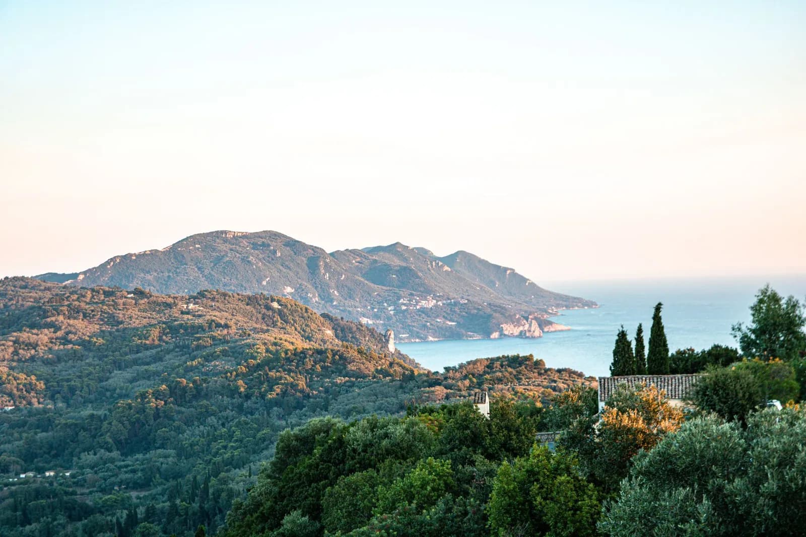The wooded west coast of Corfu at the end of the day, cypress and olive running down forested headlands to the sea