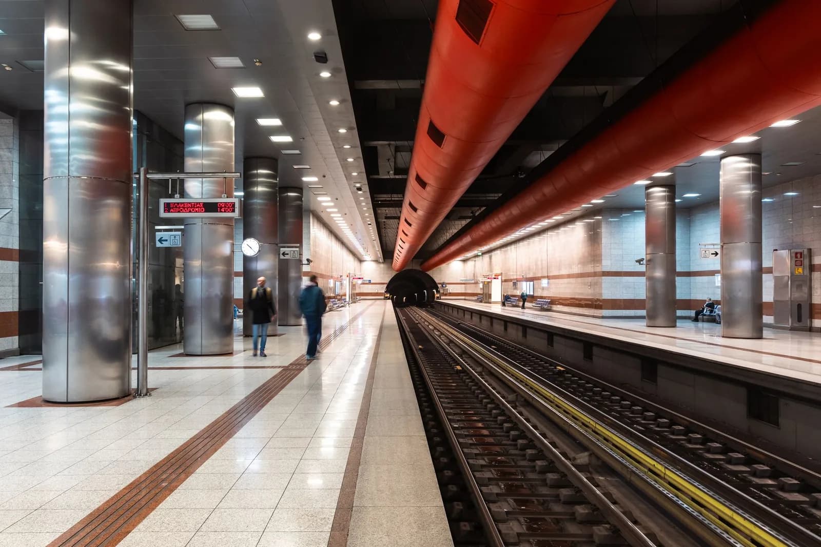 Line 3 platform on the Athens metro, with steel columns and a Greek departure screen showing trains to Plakentias and the airport