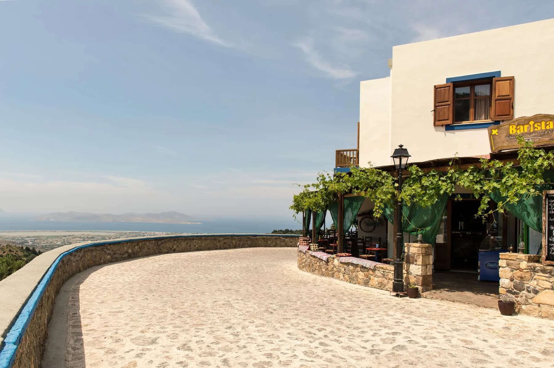 A stone-paved terrace in a hill village on Kos looking out over the flat coastal plain, the sea and a mountainous island on the horizon