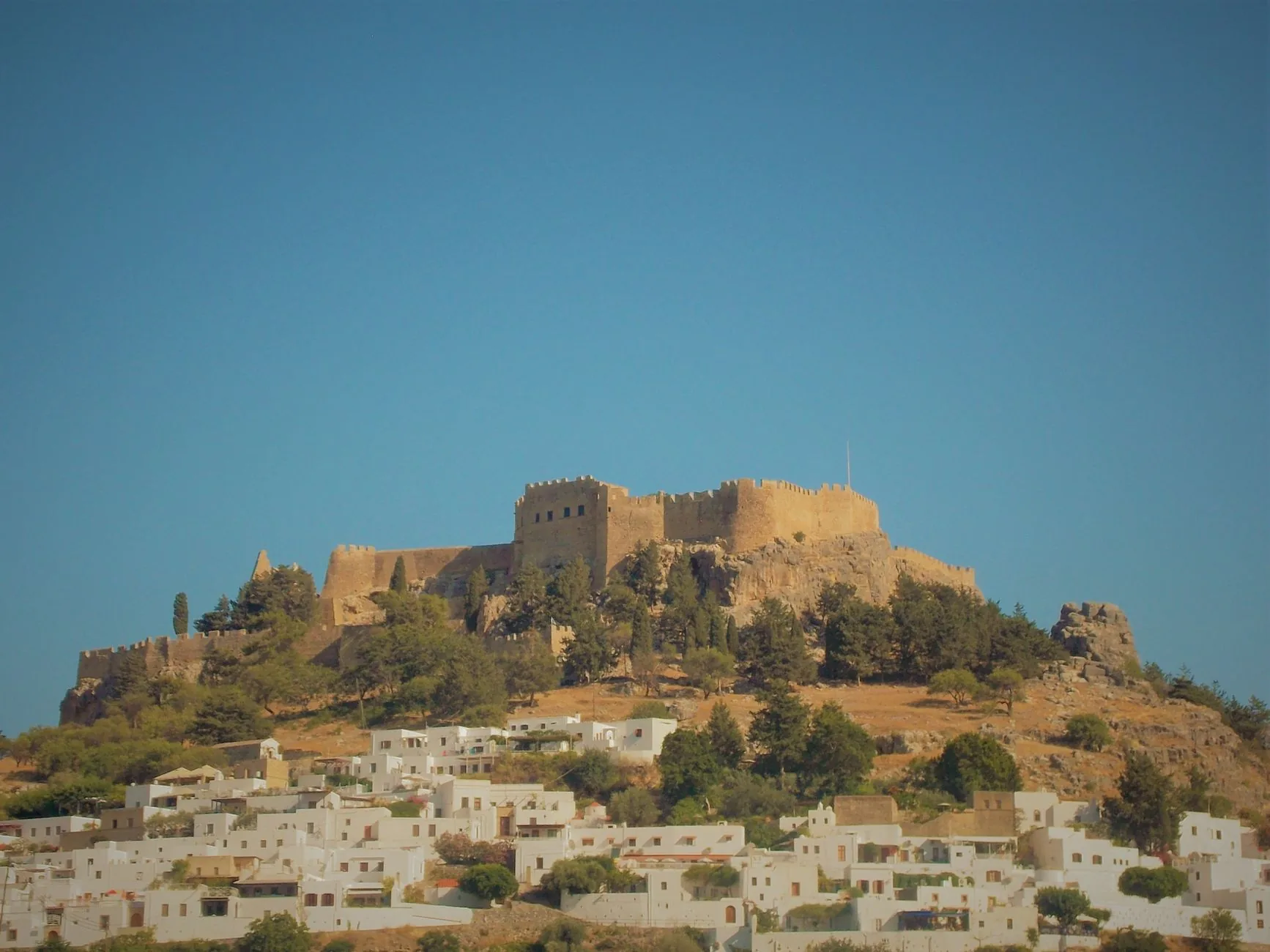 The acropolis of Lindos on Rhodes, with the crenellated castle wall of the Knights on the rock and the whitewashed cube houses of the village below it