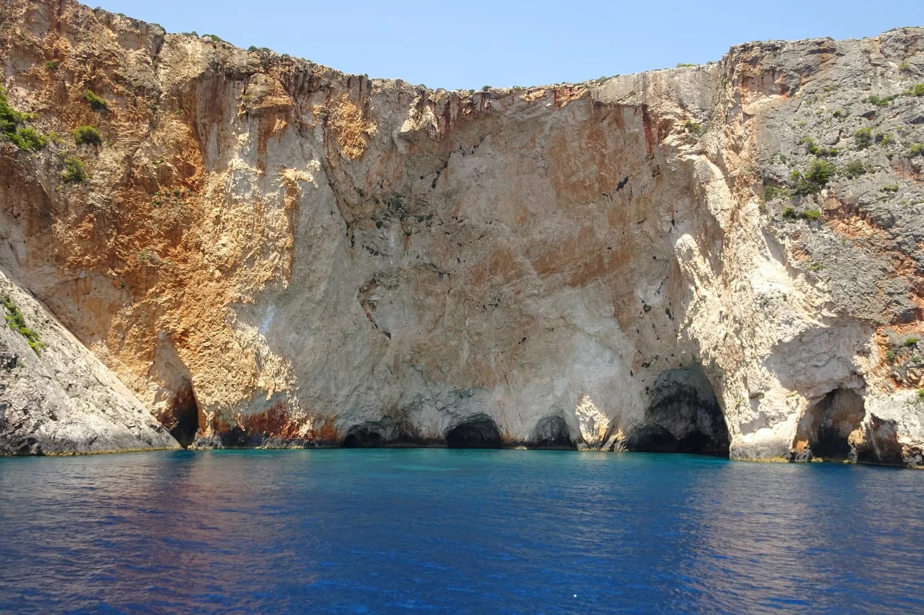 Sea caves at the waterline under the white limestone cliff wall of the west coast of Zakynthos, photographed from a boat on the open sea