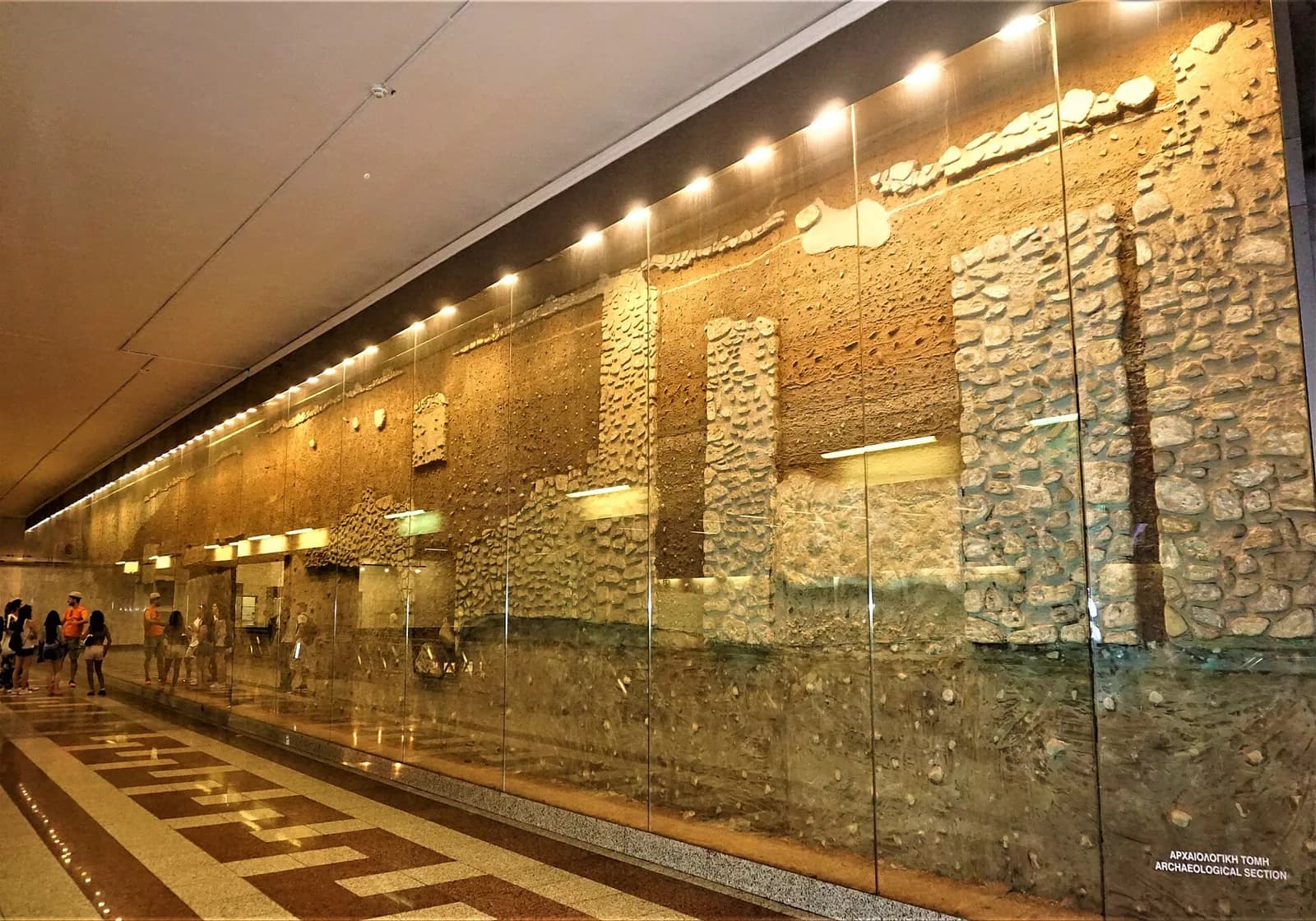 Glass-fronted archaeological section in Syntagma metro station, Athens, showing the excavated soil layers and the remains of ancient walls