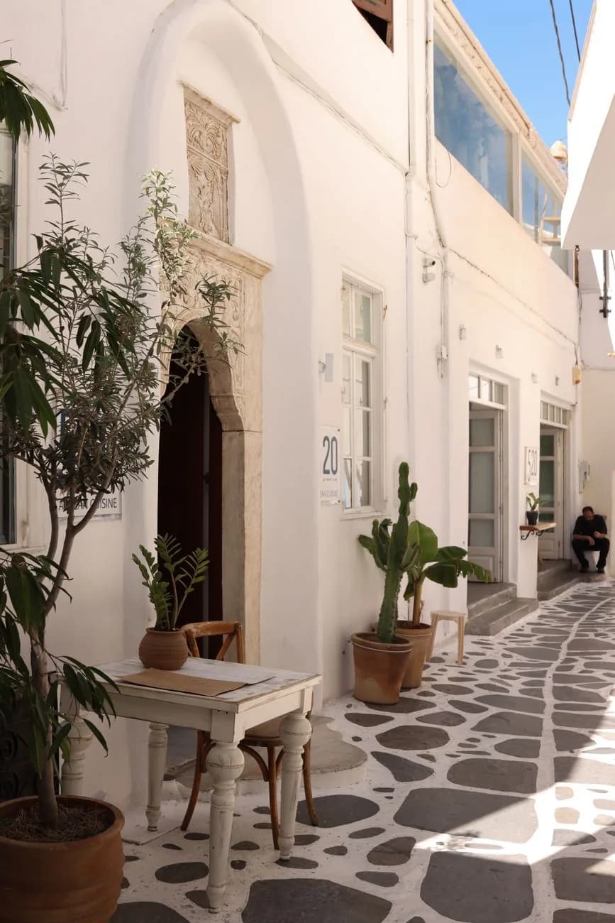 A carved marble doorway in a whitewashed lane of the old town of Naxos Chora, with potted olive trees on the flagged stone paving