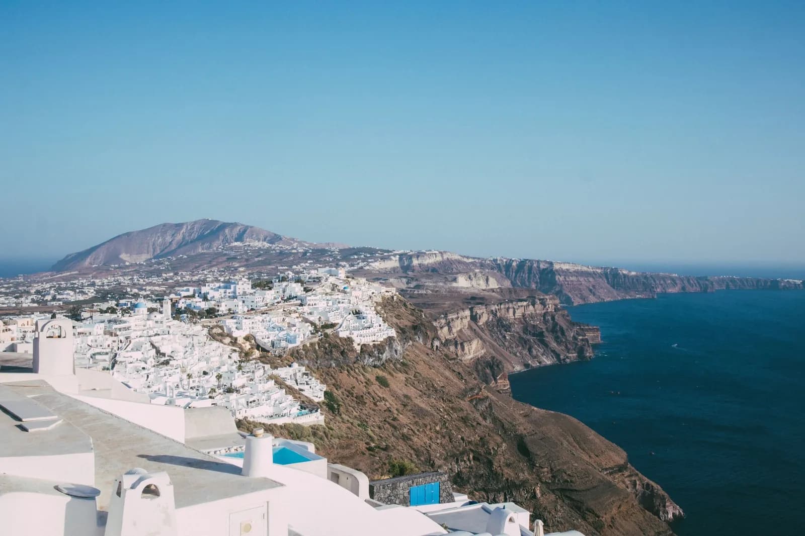 The caldera cliff of Santorini seen from Firostefani, with Fira spilling white along the rim and the crater wall dropping into the water below