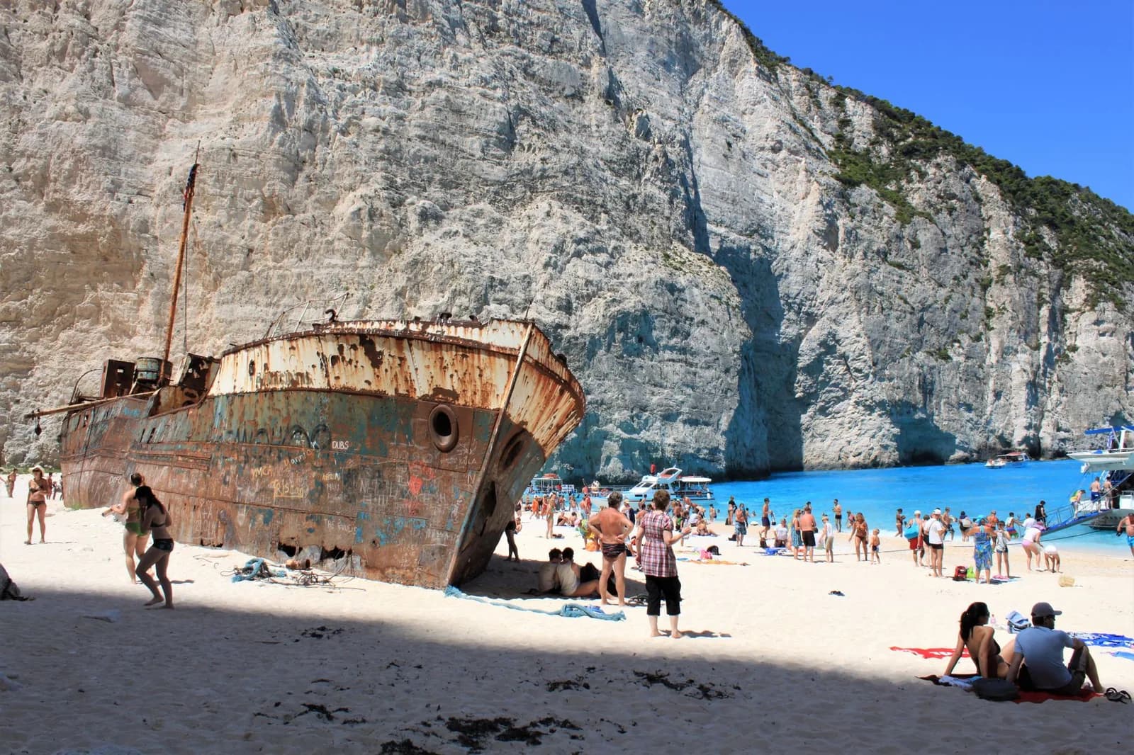 The wreck of the Panagiotis on the sand at Navagio beach, Zakynthos, between white cliffs, with tour boats moored in the turquoise cove